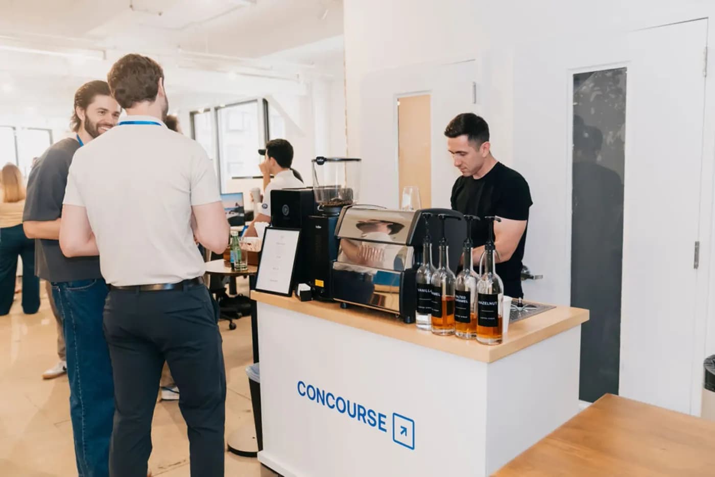 A Zerno barista preparing drinks at a branded espresso bar while guests talk in a bright office space.
