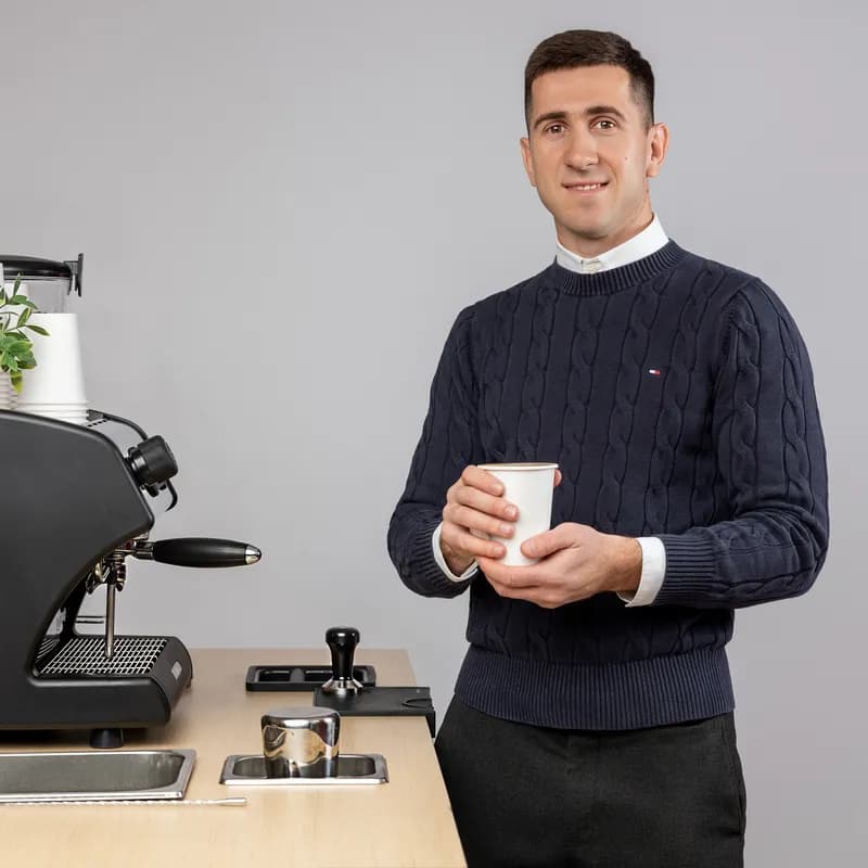 Smiling Zerno barista holding a coffee beside the espresso machine