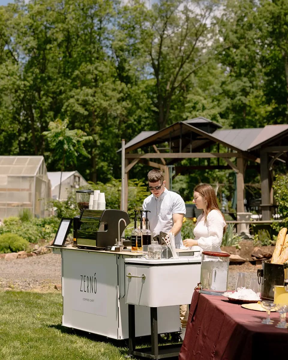 Staffed white coffee cart among garden tables and trees