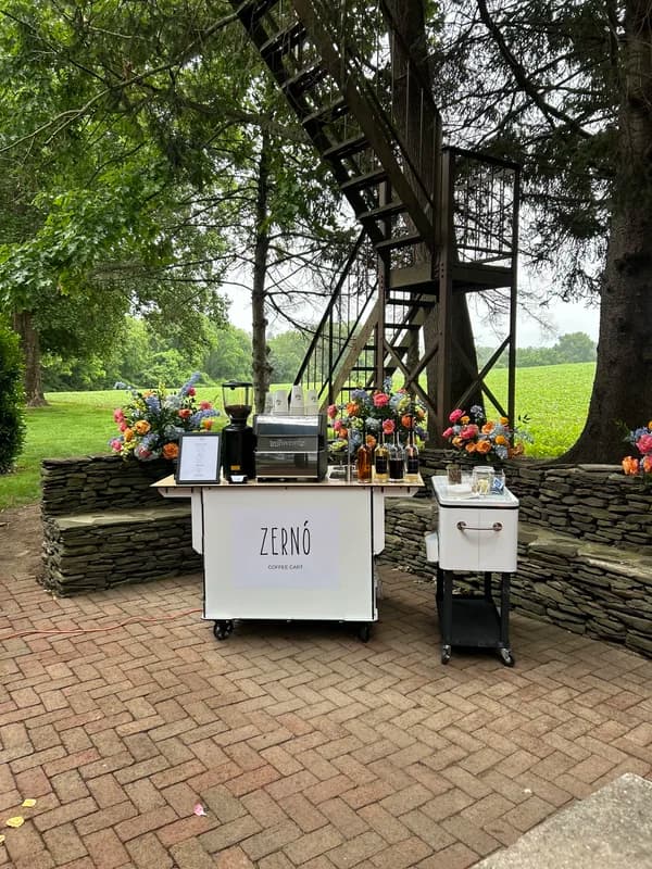 White Zerno coffee cart with flowers on a brick patio under a leafy tree